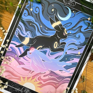 Pu&ograve; includere: Una stampa d'arte digitale con due Pok&eacute;mon, Espeon e Umbreon, in un cielo notturno stilizzato con nuvole vorticose e stelle. La stampa &egrave; incorniciata in nero.