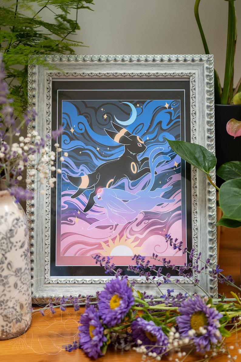 Pu&ograve; includere: Una stampa incorniciata di un personaggio Pokemon nero e blu con una luna crescente e stelle sullo sfondo. Il personaggio sta volando nell'aria con un tramonto rosa e viola in lontananza.