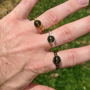 May include: Two rings with green gemstone settings. The rings are made of wire wrapped around the stones. One ring is gold and the other is silver.