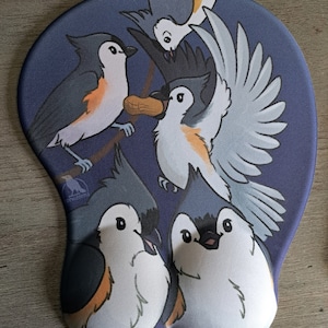 May include: A blue and white mouse mat featuring a design of four cartoon birds. The birds are all different colours and have different expressions. One bird is holding a peanut.