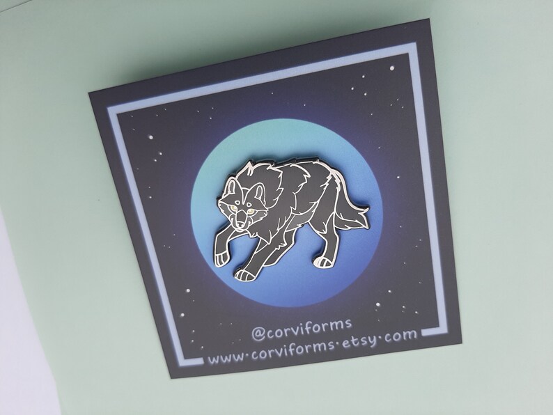 K&ouml;nnte beinhalten: Schwarze Emaille-Anstecknadel mit einem Wolf, der zum Mond heult. Die Anstecknadel ist vor einem blauen und schwarzen Sternenhimmel platziert. Die Anstecknadel tr&auml;gt den Text "@corviforms" und "www.corviforms.etsy.com".