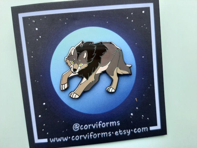 K&ouml;nnte beinhalten: Eine graue und schwarze Emaille-Anstecknadel mit einem Wolf, der zum Mond heult. Die Anstecknadel ist vor einem blauen Hintergrund mit wei&szlig;en Sternen platziert. Der Text "@corviforms" und "www.corviforms.etsy.com" befindet sich am unteren Rand der Anstecknadel.
