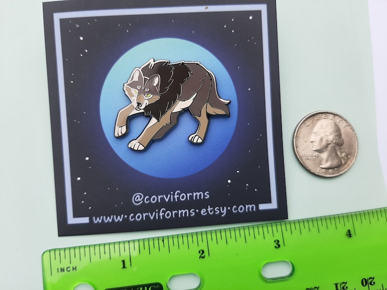 K&ouml;nnte beinhalten: Eine braune und graue Wolf-Emaille-Anstecknadel mit gelben Augen, vor einem Hintergrund aus blauem Mond mit wei&szlig;en Sternen. Die Anstecknadel hat einen Durchmesser von etwa 2,5 cm. Die Anstecknadel befindet sich auf einer wei&szlig;en Karte mit dem Text "@corviforms www.corviforms.etsy.com".