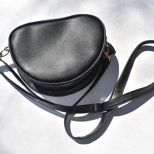 May include: A black round crossbody bag with a gold clasp and a long adjustable strap.