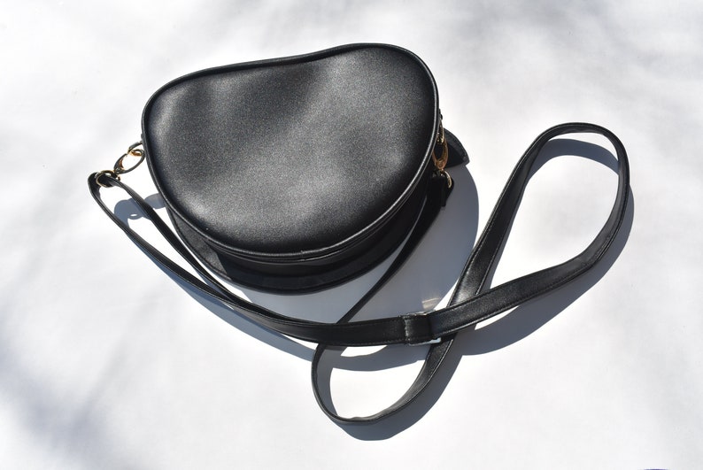 May include: A black round crossbody bag with a gold clasp and a long adjustable strap.