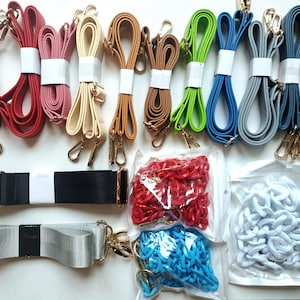 May include: An assortment of colorful bag straps and chain straps. The straps come in various colors, including red, pink, beige, brown, green, blue, gray, and black. Gold-colored metal clasps are attached to the straps. Packaged red, blue, and white chain straps are also visible.