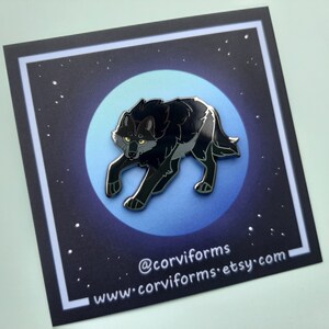 K&ouml;nnte beinhalten: Schwarze Emaille-Anstecknadel mit einem Wolf, der zum Mond heult. Die Anstecknadel ist vor einem blauen und schwarzen Sternenhimmel platziert. Die Anstecknadel tr&auml;gt den Text "@corviforms" und "www.corviforms.etsy.com".