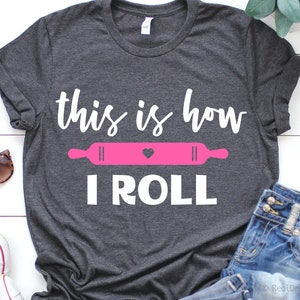 May include: A gray t-shirt with the text "this is how I ROLL" in white. A pink rolling pin with a heart is above the text.