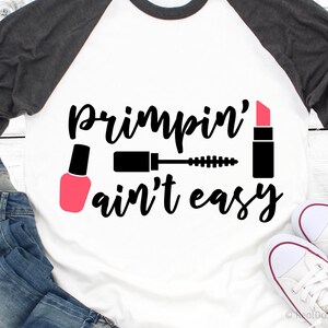 May include: A white t-shirt with a black and pink design that says "Primpin' ain't easy". The design includes a lipstick, mascara, and nail polish.