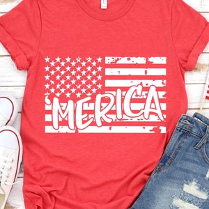 以下が含まれることがあります： 白いダメージ加工のアメリカ国旗のデザインと「MERICA」という文字がプリントされた赤いTシャツ