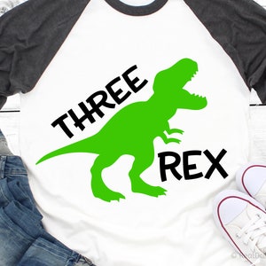 May include: A white t-shirt with a green dinosaur silhouette and the text "THREE REX" in black.