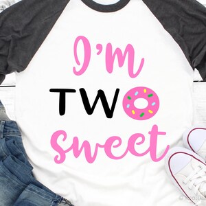 May include: A white and grey baseball tee shirt with pink lettering that says "I'm TWO sweet" and a pink donut with colorful sprinkles.