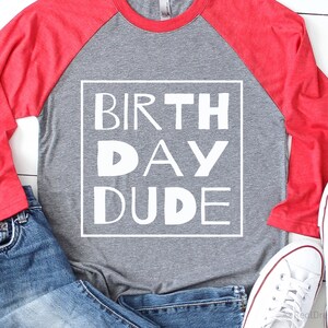 May include: A gray and red long-sleeved shirt with the text "BIRTHDAY DUDE" in a white box.