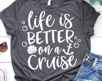 May include: A dark gray t-shirt with white text that reads "life is better on a cruise". The text is surrounded by small white circles and a seashell and anchor graphic.