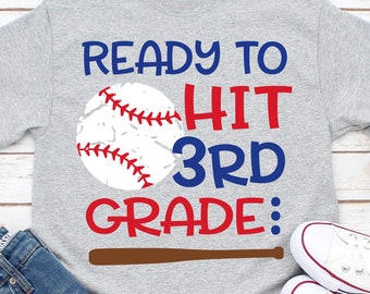 Può includere: Maglietta grigia con una grafica di baseball e il testo "Ready to Hit 3rd Grade:" in rosso e blu. Una mazza da baseball marrone è sotto il testo.