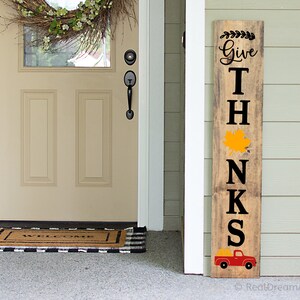 May include: A wooden sign with the words "Give Thanks" in black lettering. The sign has a red truck with a yellow leaf on the back. The sign is a fall-themed decoration.