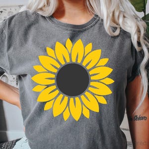 May include: A gray t-shirt with a yellow sunflower graphic. The sunflower has a dark gray center.