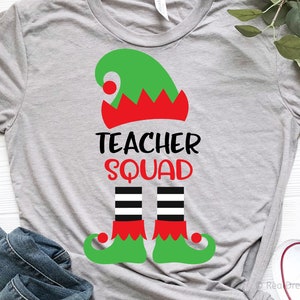 May include: A gray t-shirt with a green elf hat, red and white trim, and black and white striped elf legs. The text "Teacher Squad" is printed in black on the shirt.