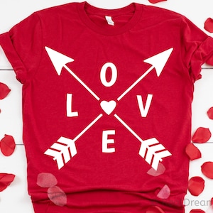 Puede incluir: Camiseta roja con flechas blancas y la palabra "LOVE" en el centro. Las flechas están cruzadas y el corazón está en el centro de la cruz.