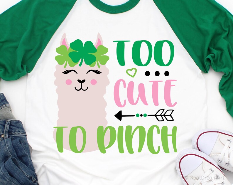 May include: A white t-shirt with a green and pink design featuring a llama with a clover crown and the text "Too cute to pinch".