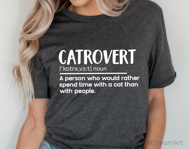 May include: Dark gray t-shirt with the word "CATROVERT" in large white letters. Below the word is the phonetic pronunciation and definition: "A person who would rather spend time with a cat than with people."