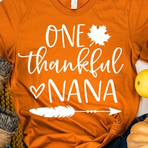 May include: Orange t-shirt with white text that reads "One thankful Nana" with a heart and a feather with an arrow.