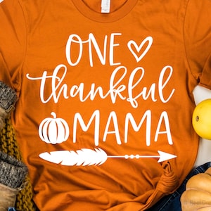 May include: Orange t-shirt with white text that reads "One ♥ thankful mama" with a pumpkin, feather, and arrow graphic.