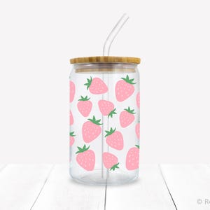 May include: A clear glass reusable tumbler with a bamboo lid and a straw. The tumbler has a pink and green strawberry pattern.