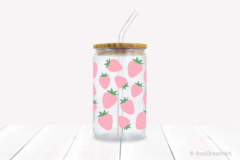 May include: A clear glass reusable tumbler with a bamboo lid and a straw. The tumbler has a pink and green strawberry pattern.