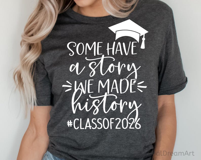 Pu&ograve; includere: T-shirt grigio scuro con testo bianco e un cappello di laurea. Il testo recita "Some have a story, we made history, #Classof2026". Una maglietta casual per le celebrazioni di laurea.