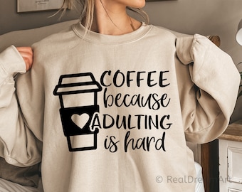May include: A beige sweatshirt with a black graphic of a coffee cup and the text "COFFEE because ADULTING is hard".