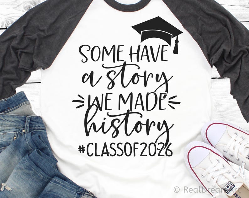 Pu&ograve; includere: Maglietta da baseball raglan bianca e grigia con la scritta "SOME HAVE a story WE MADE history #CLASSOF2026" e una grafica di cappello di laurea. La maglietta &egrave; abbinata a jeans blu e scarpe da ginnastica bianche.