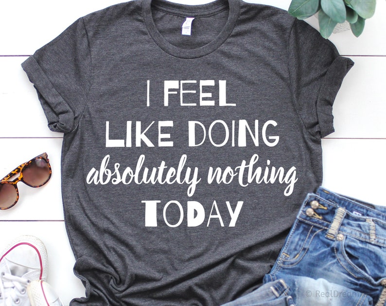 Puede incluir: Una camiseta gris oscuro con el texto "I feel like doing absolutely nothing today" impreso en blanco.