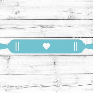 May include: A light blue rolling pin with a white heart in the center, on a white wood background.