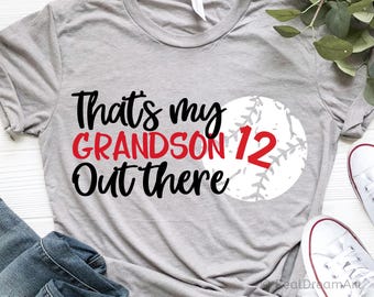 May include: Gray t-shirt with black text that reads "That's my grandson 12 out there" and a white baseball with red stitching and the number 12.