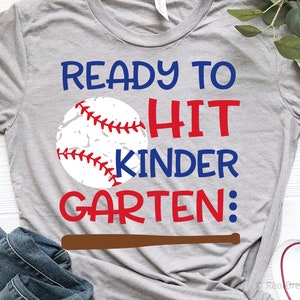 May include: Grey t-shirt with a baseball graphic and the text "Ready to Hit Kinder Garten:" in red and blue lettering. A brown baseball bat is below the text.