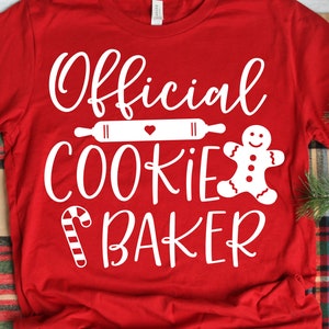 May include: Red t-shirt with white text that reads "Official Cookie Baker". The text is decorated with a rolling pin, a gingerbread man, and a candy cane.