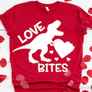 May include: Red t-shirt with a white dinosaur silhouette holding a heart with a bite taken out of it. The text "LOVE BITES" is printed on the shirt.