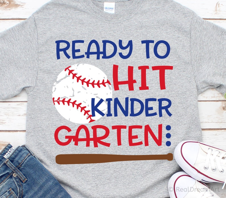 May include: Grey t-shirt with the text "Ready to Hit Kinder Garten:" in red and blue lettering. A baseball with red stitching is next to the text. A brown baseball bat is below the text.