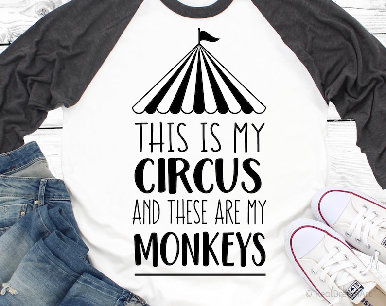 Op de afbeelding: Een wit en grijs raglan t-shirt met een zwart-witte afbeelding van een circus tent en de tekst "This is my circus and these are my monkeys".