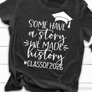 Pu&ograve; includere: T-shirt nero con testo bianco: "SOME HAVE a story WE MADE history #CLASSOF2026" e grafica di cappello di laurea. Un paio di occhiali da sole neri sono appoggiati sul lato della maglietta piegata.