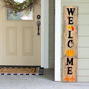 以下が含まれることがあります： 黒い文字で「WELCOME」と書かれた木製のウェルカムサイン。サインは七面鳥、カボチャ、七面鳥の足で飾られています。