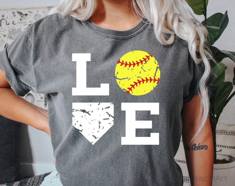 May include: A gray t-shirt with the word "LOVE" printed in white. The "O" is replaced with a yellow softball with red stitching. The "V" is replaced with a white silhouette of a baseball home plate.