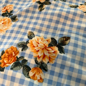 May include: A blue and white gingham fabric with a floral pattern. The flowers are orange and yellow with green leaves.