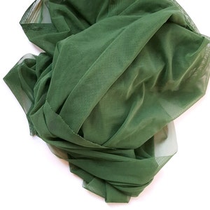 May include: Dark green tulle fabric, gathered and draped, forming soft folds and shadows. The fabric has a fine mesh texture, and the edges are neatly finished. The material is opaque and appears to be a lightweight textile, suitable for various craft projects.