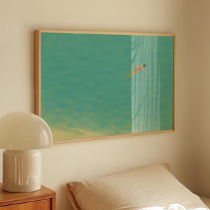 May include: A framed print shows a swimmer in turquoise water. The artwork is in a light wood frame, above a bed with cream linens. A white mushroom lamp sits on a wooden bedside table. The room has a neutral colour palette.