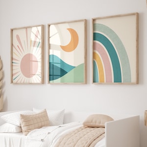 May include: Three framed abstract art prints with a sun, moon, and rainbow design in a nursery with a white daybed and a rocking horse.