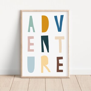 May include: A framed art print with the word "ADVENTURE" in colorful, block letters. The letters are in shades of blue, green, yellow, brown, and pink against a white background. The frame is a light wood color, and the print is displayed on a wooden floor.