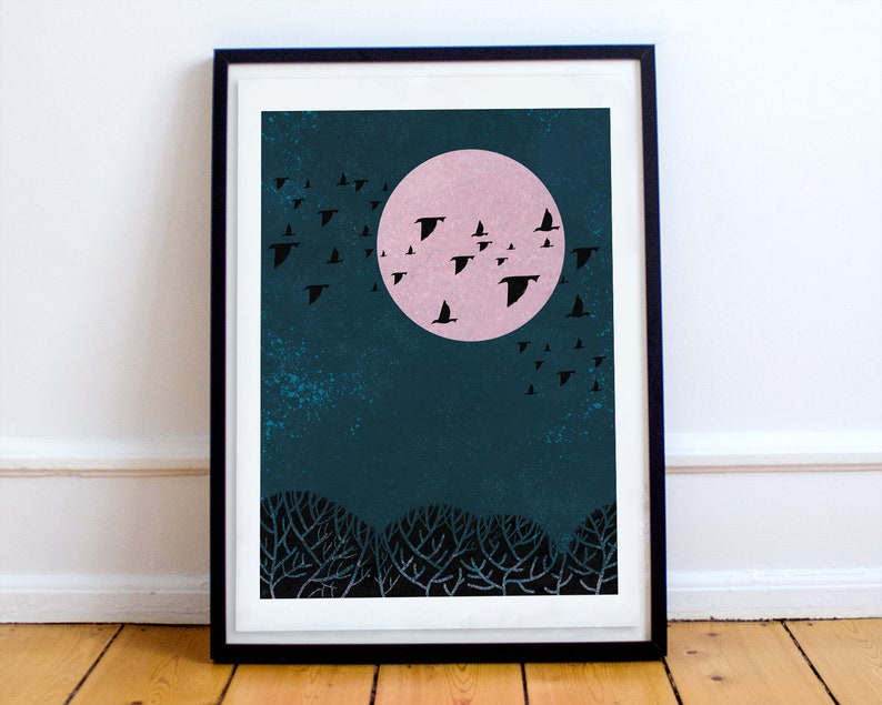 May include: A framed print of a minimalist illustration of a flock of birds flying in front of a large pink moon against a dark blue background. The birds are black silhouettes and the moon is a solid pink circle. The background is a dark blue with a textured look.