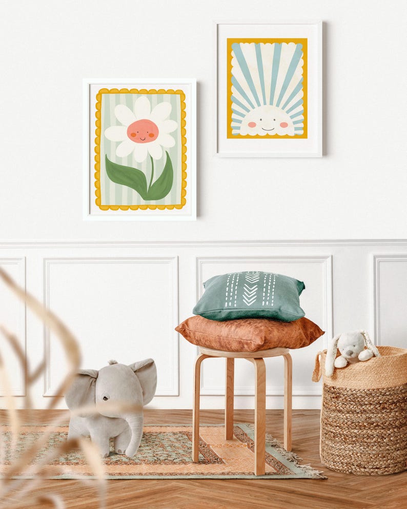 May include: Two framed illustrations, one of a smiling flower and the other of a smiling sun, hang on a white wall. A wooden stool with a green and brown pillow sits in front of a woven basket with a stuffed animal inside.